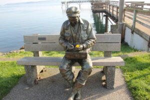 Sculpture of old man by the sea with his hands over a lunch box